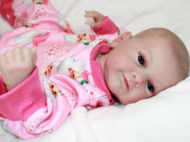 A baby doll wearing pink pajamas is positioned on a bed, highlighting a serene and nurturing environment.